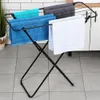 A black foldable drying rack with several towels draped over it, set against a tiled wall and floor. Voir les images du produit