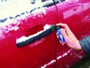 A person is spraying a car door handle with a de-icing spray in snowy weather. Produktbild-Vorschau