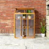 A wooden greenhouse with plants inside, placed on a tiled patio in front of a brick wall. Náhľad obrázku produktu