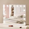 A vanity mirror with lights is placed on a surface in front of a bed. Podgląd zdjęcia produktu