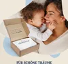 A mother and baby are shown in a warm, intimate moment, with a product box open in the foreground. Produktbild-Vorschau
