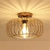 A close-up shot of a gold-colored ceiling light fixture with a cage-like design and an exposed Edison bulb, mounted on a white ceiling. Náhled obrázku produktu