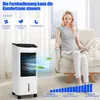 A woman sits in a chair holding a remote control, looking at a portable air cooler in a living room setting. Produktbild-Vorschau