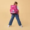 A young girl wearing a pink backpack and striped pants stands against a plain yellow background. Anteprima dell’immagine prodotto