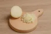 A half-cut onion and chopped onions are placed on a small wooden cutting board, which is on a wooden surface. Produktbild-Vorschau