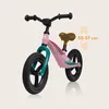 A pink balance bike with teal accents and a brown seat, shown from a front-side angle against a light beige background. Produktbild-Vorschau