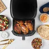 An air fryer filled with cooked chicken breasts, surrounded by various side dishes and utensils. Produktbild-Vorschau