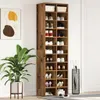 A tall, narrow shoe cabinet with multiple shelves filled with shoes and storage boxes, placed next to a large potted plant and a door. Anteprima dell’immagine prodotto