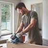 A man is using a Bosch cordless planer to smooth a piece of wood. Podgląd zdjęcia produktu