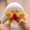 A close-up shot of a cute, white silicone duck-shaped night light with yellow feet and a red tongue, being held by two hands. Produktbild-Vorschau