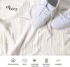 A flat lay of white sneakers on a textured white fabric, with a logo and icons at the bottom. Produktbild-Vorschau