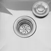 A close-up view of a stainless steel sink drain with a removable strainer and a matching drain cover. Produktbild-Vorschau
