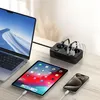 A black power strip with multiple USB ports is charging a laptop, tablet, and smartphone on a wooden desk. Anteprima dell’immagine prodotto