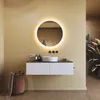 A modern bathroom vanity with a round illuminated mirror, sink, and storage. A laundry basket and plant are also visible. Podgląd zdjęcia produktu