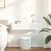 A white floating shelf with two drawers is mounted on a white wall above a white cylindrical stool. A vase with dried flowers sits on the shelf, and a large green plant is visible to the right. Podgląd zdjęcia produktu