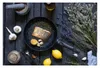 A cooked salmon fillet in a frying pan with lemon and garlic, surrounded by ingredients and kitchen tools on a dark wooden surface. Anteprima dell’immagine prodotto