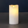 A white LED candle with a flickering yellow flame sits on a dark surface against a dark blue background. Produktbild-Vorschau