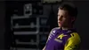 A man wearing a purple and yellow racing shirt, looking to the side. Produktbild-Vorschau