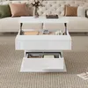 A white high-gloss coffee table with lift-top and drawers is shown in a living room setting. Produktbild-Vorschau