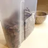 A close-up shot of a clear plastic food storage container filled with chocolate-flavored cereal, with a textured bowl in the background. Produktbild-Vorschau
