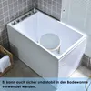A white bathtub with a gray tiled wall and a white blind in the background. A round, gray shower stool is placed inside the bathtub. Produktbild-Vorschau