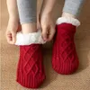 Rote gestrickte Hausschuhe-Socken mit weißem Kunstfellfutter, getragen an den Füßen einer Person, auf strukturierter brauner Oberfläche Náhľad obrázku produktu