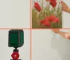 A person is hanging a picture on a wall, guided by a laser level. Produktbild-Vorschau