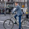 A man in a suit and jeans rides an e-bike through a city street. Produktbild-Vorschau