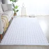 A white fluffy rug is laid out on a wooden floor in a living room setting, next to a sofa. Produktbild-Vorschau