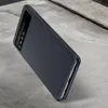 A dark gray smartphone case with a transparent window is shown at an angle on a textured gray surface. Náhled obrázku produktu