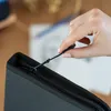 A hand is shown closing a black zipper on a black case. Podgląd zdjęcia produktu