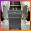 A gray suitcase is placed on a metallic floor in front of an escalator. Náhled obrázku produktu