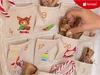 A hand is shown reaching into a fabric advent calendar filled with small brown paper-wrapped gifts. Produktbild-Vorschau