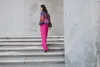 A woman walks up a set of concrete stairs, wearing a colorful sweater and pink pants. Produktbild-Vorschau