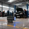 A workshop or garage setting with mechanics working on a car and a heater in the foreground. Produktbild-Vorschau