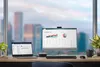 A desk setup with a laptop and a monitor displaying spreadsheets, overlooking a city skyline. Produktbild-Vorschau