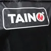 A close-up of a black fabric with a white logo that says TAINO with a flame symbol. Produktbild-Vorschau