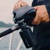 A person is holding a black electric fishing reel with a battery pack attached, on a boat with water and hills in the background. Náhled obrázku produktu