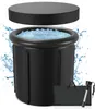 A black inflatable ice bath with a lid, filled with water and ice, surrounded by water splashes. A black carrying bag and a flashlight are placed in front of the bath. Produktbild-Vorschau