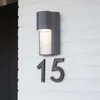 A modern outdoor wall light mounted on a white brick wall, with house numbers '15' below it. Anteprima dell’immagine prodotto