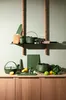 A collection of green kitchenware items arranged on a wooden countertop and a shelf against a light gray wall. Produktbild-Vorschau