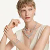 A woman wearing a white dress and multiple pieces of Swarovski jewelry, including necklaces, earrings, bracelets, and rings. Produktbild-Vorschau