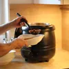 A person is serving soup from a large black soup kettle into a white bowl. Produktbild-Vorschau