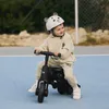 A young child wearing a bear-themed helmet and beige tracksuit rides a black 6-in-1 tricycle on a blue court. Voir les images du produit