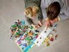 A father and daughter are playing with LEGO bricks on the floor, following instructions from a booklet. Produktbild-Vorschau