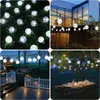 A collage of four images showing solar-powered LED string lights in various outdoor settings, including on grass, attached to a building, over a gazebo, and draped over trees above a dining table. Náhled obrázku produktu