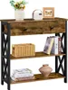 A narrow console table with a rustic, industrial design, featuring a wooden top with a drawer, and two open shelves below. It is decorated with a vase of flowers, a small radio, a framed picture, a woven basket, books, and a decorative vase. Produktbild-Vorschau