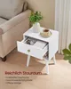 A white nightstand with an open drawer, a cup of coffee, and a plant on top, placed next to a sofa. Produktbild-Vorschau