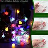A string of colorful LED lights wrapped around a glass bottle and a decorative object, with inset images showing how to insert batteries. Produktbild-Vorschau