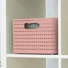 A pink storage basket with a woven pattern sits on a white shelf. Voir les images du produit